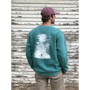 Young male wearing a tropical timid teal sweatshirt with the Kayak design by Chillwater. The back resembles a a kayaker floating down a river surrounded by trees.