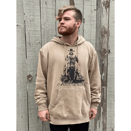 Young male wearing a cobblestone khaki hooded sweatshirt in the Rawhide design by Chillwater. The front pictures a cowboy on horseback.