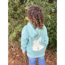 Young child wearing a tropical timid teal hoodie sweatshirt with the Kayak design from Chillwater Apparel. The back resembles a kayaker floating down a river covered by trees. 