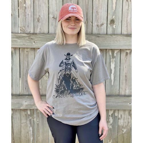Young female wearing a concho steal grey short sleeve tee in the Rawhide design by Chillwater. The front pictures a cowboy riding horseback.