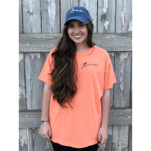Young woman wearing orange chillwater tshirt with angler design. Design features fly fisherman wading in a body of water.