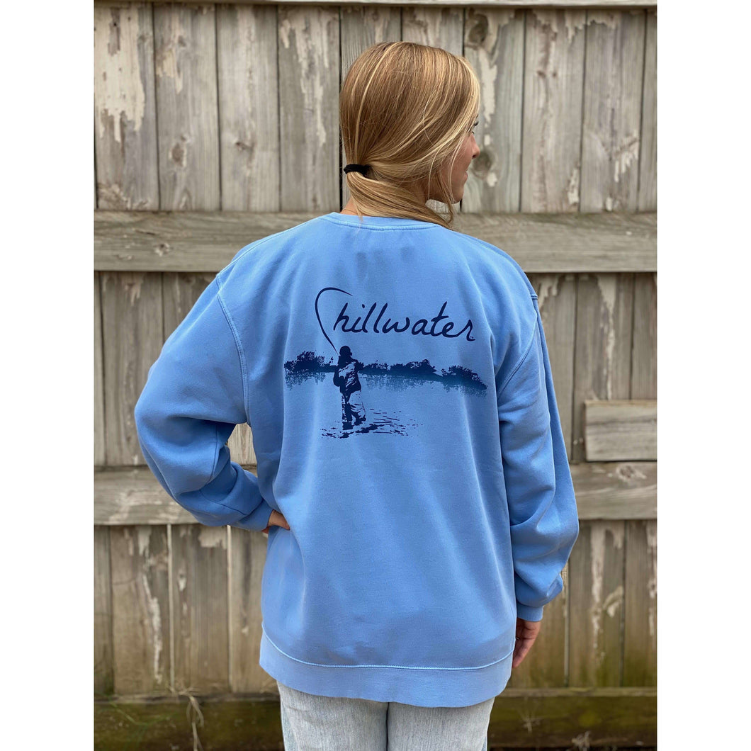 Young woman in blue chillwater sweatshirt with angler fishing design on the back. Design features fly fisherman wading in a body of water.