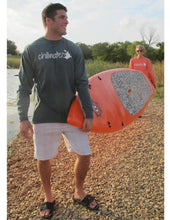 Male and female wearing Kayak long sleeve tees by Chillwater in trees of evergreen and flamingo orange colors, carrying a paddle board on a rocky beach.