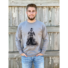 Young male wearing a concho steal grey long sleeve tee in the Rawhide design by Chillwater. The front pictures a cowboy on horseback.