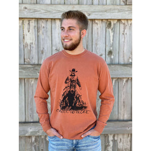 Young male wearing a wagon wheel rust long sleeve tee in the Rawhide design by Chillwater. The front pictures a cowboy on horseback.
