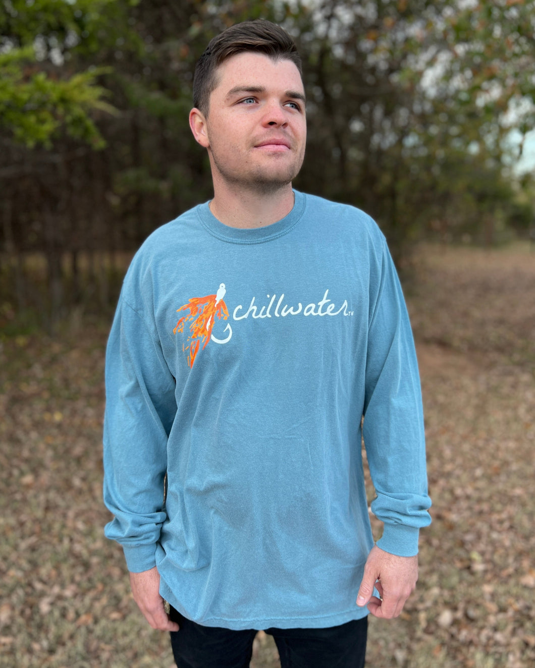 Young male wearing a cornflower blue long sleeve tee Hook and Fly design by Chillwater. The front resembles a fishing hook and fly with Chillwater written across.