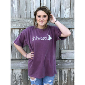 Young female wearing a dark leaf magenta short sleeve tee with the Kayak design by Chillwater. The back resembles a kayaker floating down a river covered by trees.