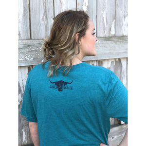 Young female wearing an aruba teal v-neck tee with the Highlander design by Chillwater. The front resembles a western portrait of a Highlander cow.