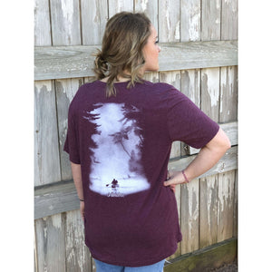 Young female wearing a dark leaf magenta short sleeve tee with the Kayak design by Chillwater. The back resembles a kayaker floating down a river covered by trees.