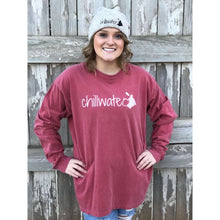 Young female wearing a faded firecracker red long sleeve tee with the Kayak design by Chillwater.The back resembles a kayaker floating down a river covered by trees.