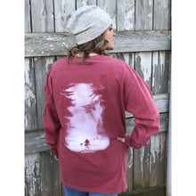 Young female wearing a faded firecracker red long sleeve tee with the Kayak design by Chillwater.The back resembles a kayaker floating down a river covered by trees.