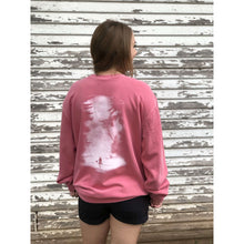 Young female wearing a pink sweatshirt with the Kayak design by Chillwater. The back resembles a kayaker floating down a river covered by trees.