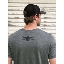 Young male wearing a barn metal grey short sleeve tee with the Highlander design by Chillwater. The front resembles a western portrait of a Highlander cow.