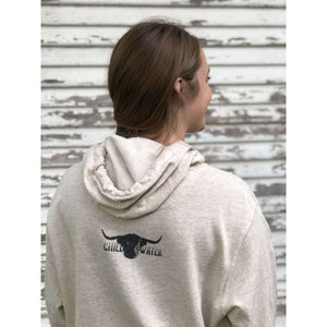 Young female wearing a washed ivory with black Highlander design on a hoodie by Chillwater. The front resembles a western portrait of a Highlander cow.