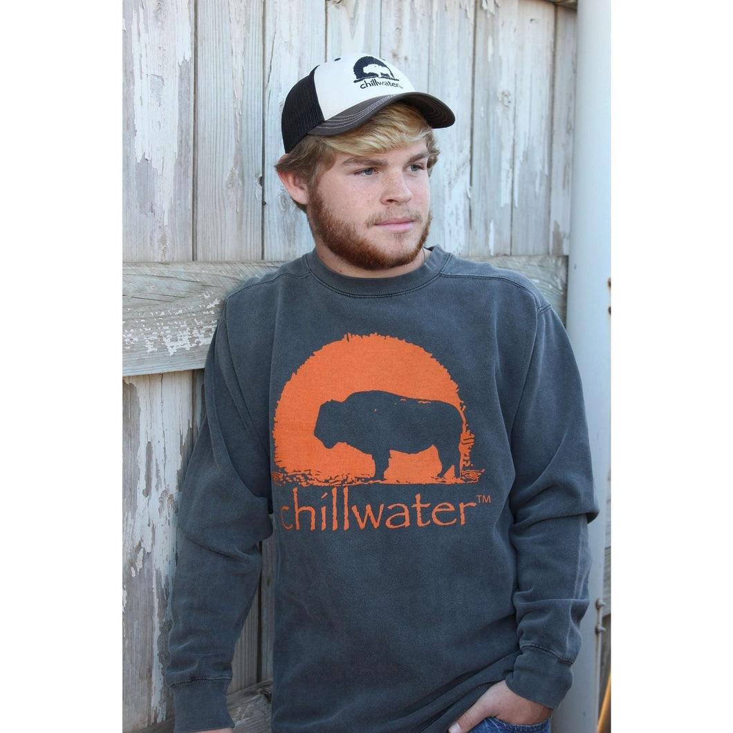 Young man wearing stone grey and orange Buffalo sweatshirt by Chillwater in front of a rustic white fence.