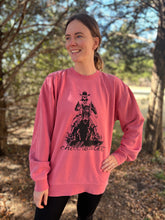 Young male wearing a faded pink sweatshirt in the Rawhide design by Chillwater. The front pictures a cowboy on horseback.