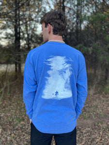 Young male wearing a Tahoe blue long sleeve tee with the Kayak design by Chillwater.The back resembles a kayaker floating down a river covered by trees.
