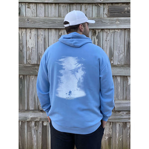 Young male wearing a soothing blue sweatshirt hoodie with the Kayak design by Chillwater. The back resembles a kayaker floating down a river covered by trees.