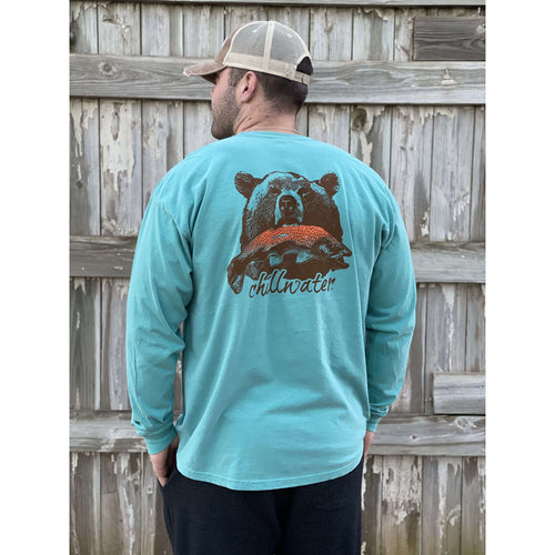 Young male wearing a tropical timid teal long sleeve tee in the Grizzly design by Chillwater. The back pictures a grizzly bear with a bright pink salmon in its mouth.