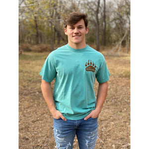 Young male wearing a tropical timid teal short sleeve tee in the Grizzly design by Chillwater. The back pictures a grizzly bear with a bright pink salmon in its mouth.