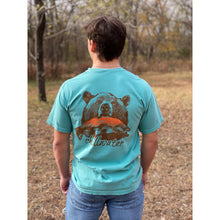 Young male wearing a tropical timid teal short sleeve tee in the Grizzly design by Chillwater. The back pictures a grizzly bear with a bright pink salmon in its mouth.