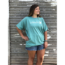 Young female wearing a tropical timid teal short sleeve tee with the Kayak design by Chillwater. The back resembles a kayaker floating down a river covered by trees.