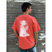  Young male wearing a flamingo orange short sleeve tee with the Kayak design by Chillwater. The back resembles a kayaker floating down a river covered by trees.
