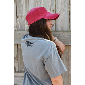 Young female wearing a barn grey short sleeve tee with the Highlander design by Chillwater. The front resembles a western portrait of a Highlander cow.