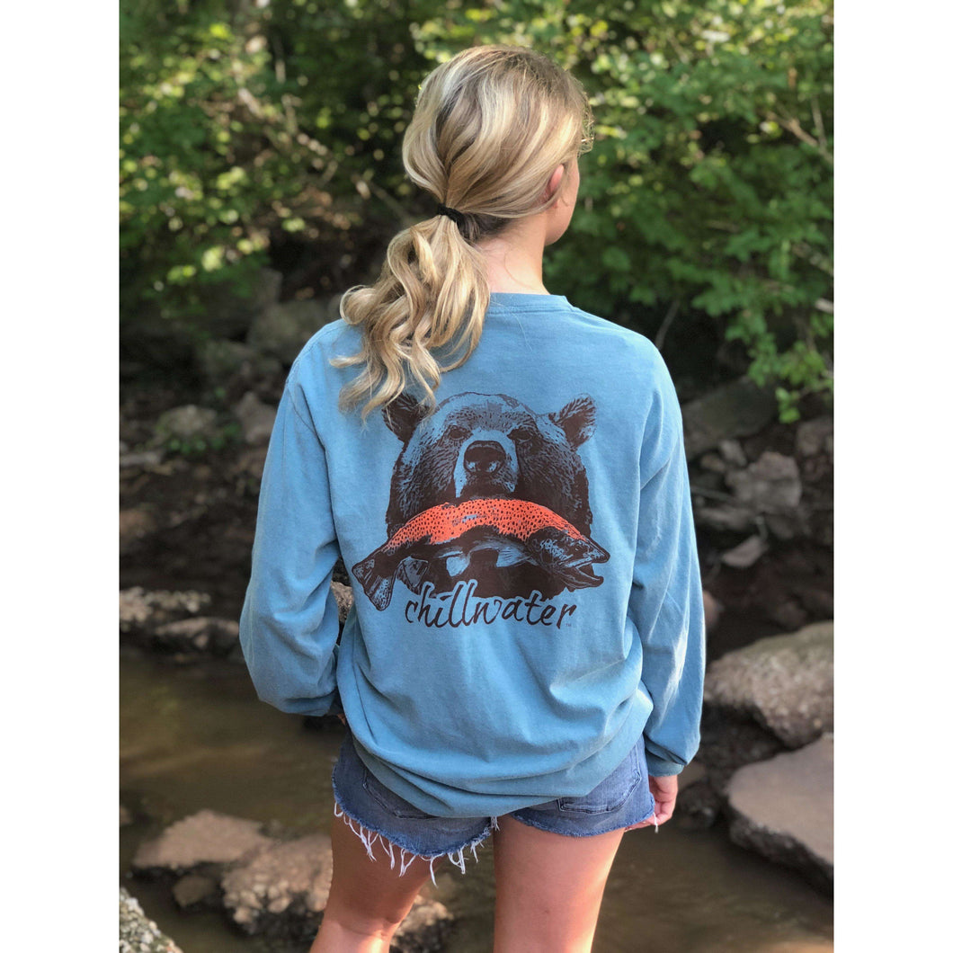 Young female wearing a cornflower blue long sleeve tee in the Grizzly design by Chillwater. The back pictures a grizzly bear with a bright pink salmon in its mouth.