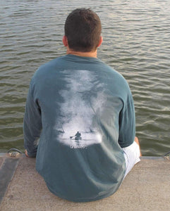 Young male wearing a along the river blue long sleeve tee with the Kayak design by Chillwater.The back resembles a kayaker floating down a river covered by trees.