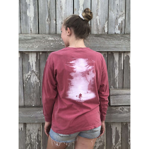 Young child wearing a faded firecracker red long sleeve with the Kayak design from Chillwater Apparel. The back resembles a kayaker floating down a river covered by trees. 