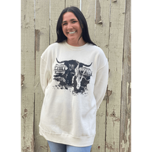 Young female wearing a soft ivory with black Highlander design on a hoodie by Chillwater. The front resembles a western portrait of a Highlander cow.