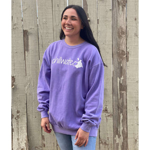 Young female wearing a orchid purple sweatshirt with the Kayak design by Chillwater. The back resembles a kayaker floating down a river covered by trees.