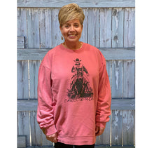 Young male wearing a faded pink sweatshirt in the Rawhide design by Chillwater. The front pictures a cowboy on horseback.