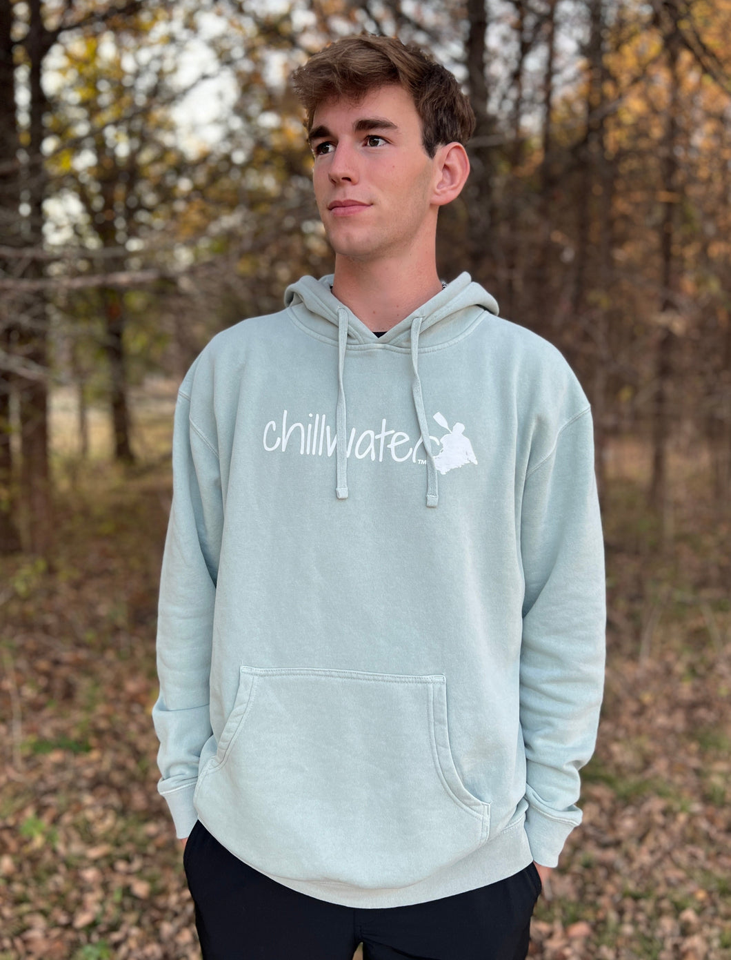 Young male wearing a soft cypress green sweatshirt hoodie with the Kayak design by Chillwater.