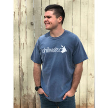Young male wearing an along the river blue short sleeve tee with the Kayak design by Chillwater. The back resembles a kayaker floating down a river covered by trees.