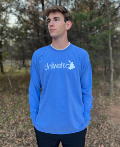 Young male wearing a Tahoe blue long sleeve tee with the Kayak design by Chillwater.The back resembles a kayaker floating down a river covered by trees.