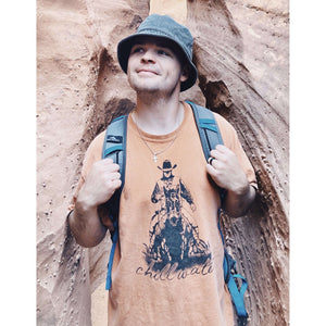 Young male wearing a wagon wheel rust short sleeve tee in the Rawhide design by Chillwater. The front pictures a cowboy on horseback.