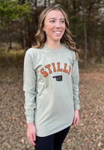 Young female wearing a cobblestone khaki long sleeve tee in the Stilly design by Chillwater Apparel. The front shows the words “Stilly” with the state of Oklahoma and a star over Stillwater.