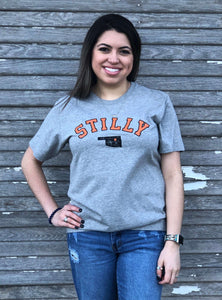 Grey short sleeve super soft t-shirt with chillwater stilly design in orange and small black oklahoma with orange star on stillwater location.