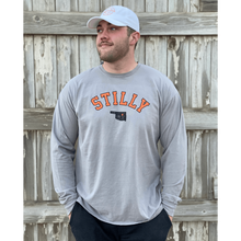 Young male wearing a lava grey long sleeve tee in the Stilly design by Chillwater Apparel. The front shows the words “Stilly” with the state of Oklahoma and a star over Stillwater.