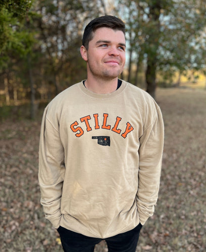 Young male wearing a Stilly design sweatshirt in Khaki color by Chillwater Apparel. The front shows the words “Stilly” with the state of Oklahoma and a star over Stillwater.